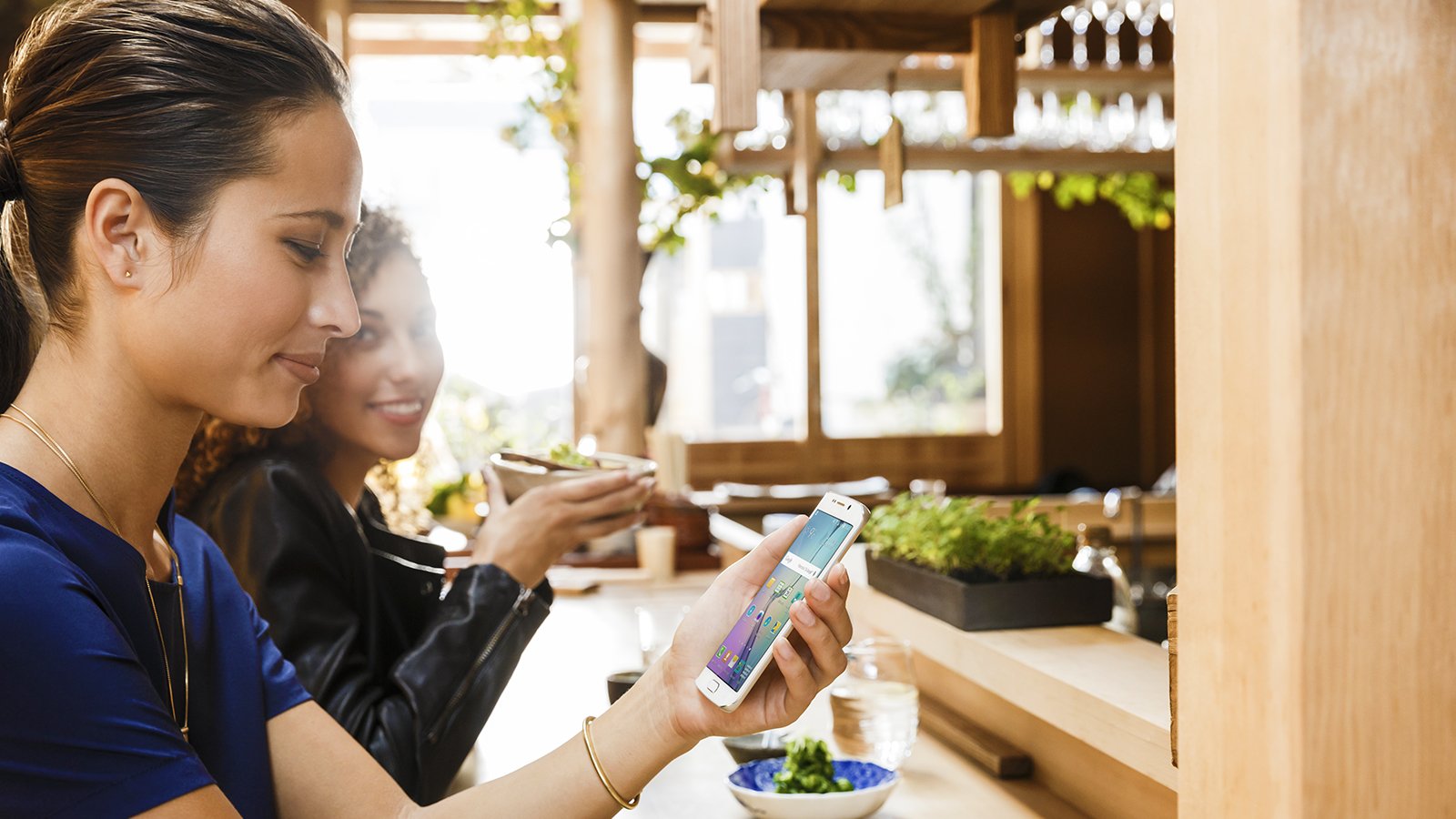 Woman holding smart phone chatting with another woman at bar.