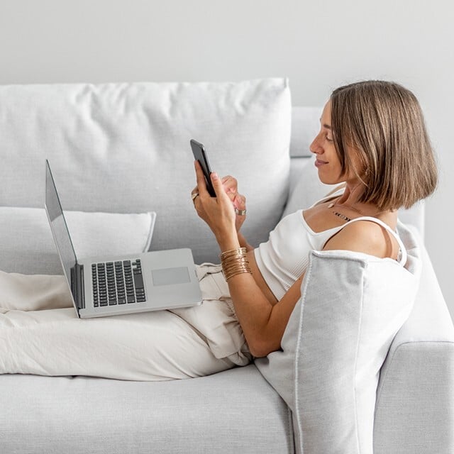woman on sofa using phone and laptop