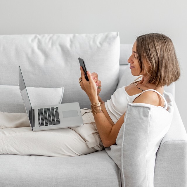 woman on sofa using phone and laptop